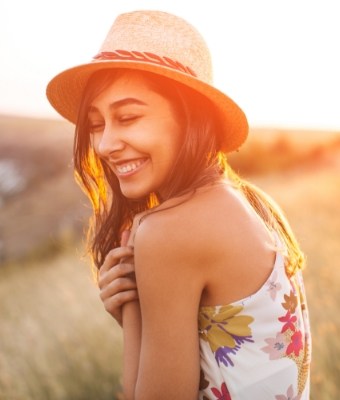 Smiling young woman in fedora outdoors at sunset
