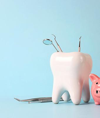 Piggy bank next to model of tooth holding dental tools