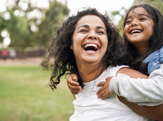 Laughing mother giving young daughter piggyback ride outside
