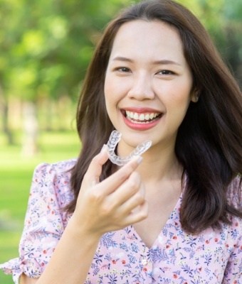 Smiling woman holding a clear aligner for SureSmile in Claremore