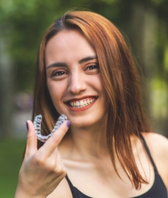 Smiling young woman holding a clear aligner outdoors